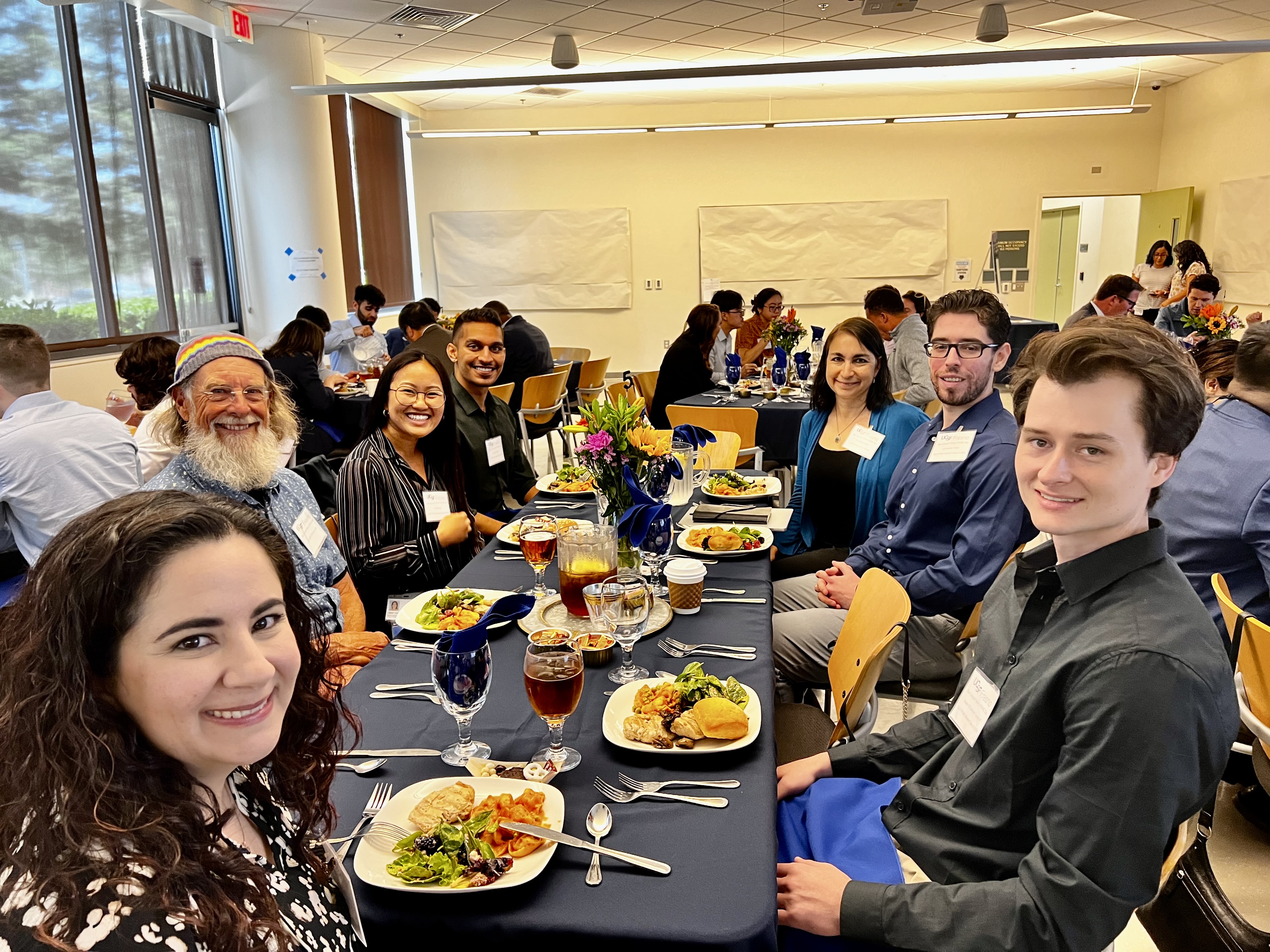 Group of people posing for a picture about to eat lunch in a cafeteria setting.