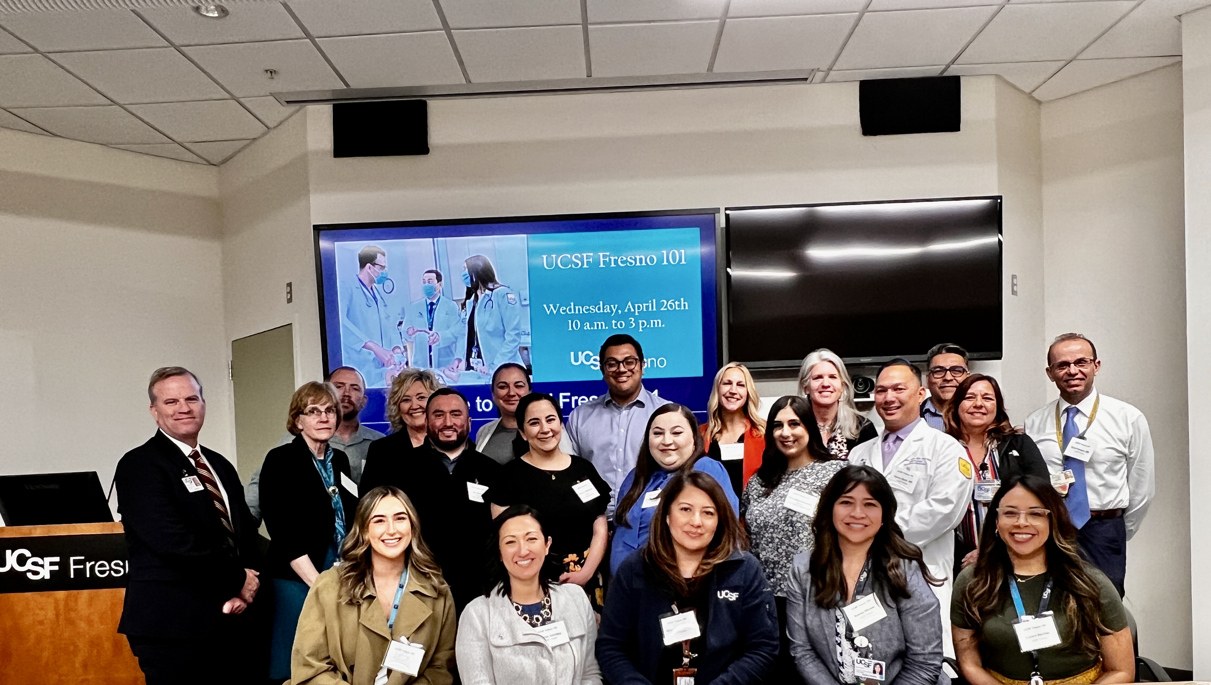 Group of people in a classroom taking a group photo in front of a presentation screen